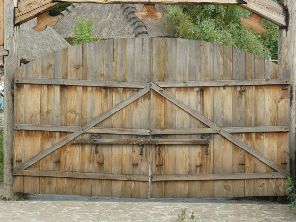 Large wooden gates in light grey tone with arching top and crossbar at center.